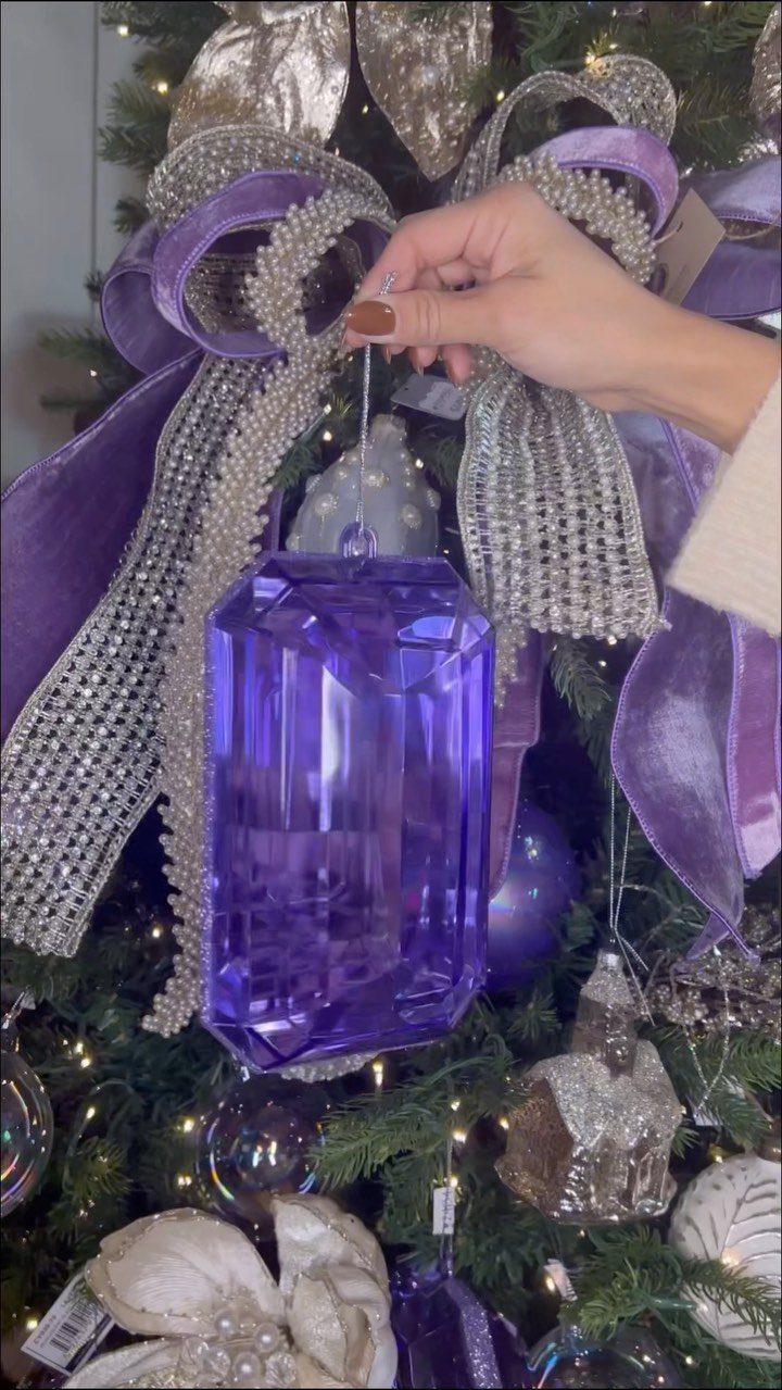 90s Christmas Tree Decor: 8 Ideas for Retro Holiday Charm 4 A hand holds a large, purple, translucent gem-shaped ornament on a decorated Christmas tree.