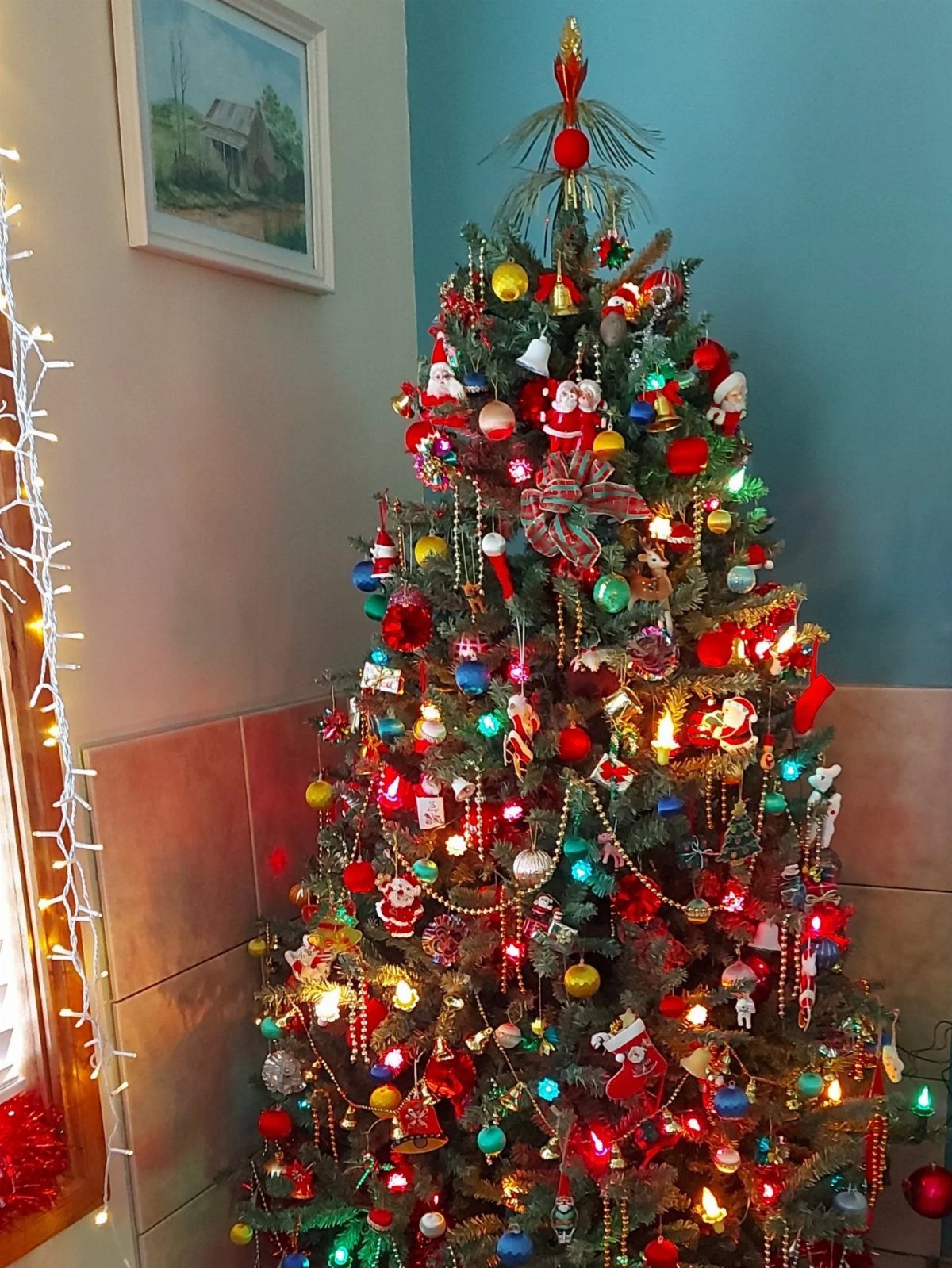 90s Christmas Tree Decor: 8 Ideas for Retro Holiday Charm 8 A decorated Christmas tree with colorful ornaments and gold bead garlands against a blue wall.