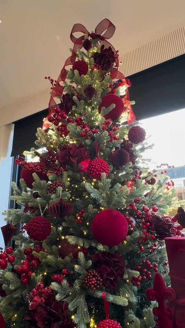 All Red Christmas Tree Decorations: 7 Ideas for Monochrome Style 4 A decorated Christmas tree with red baubles, red ribbons, and red berry picks under warm lights.