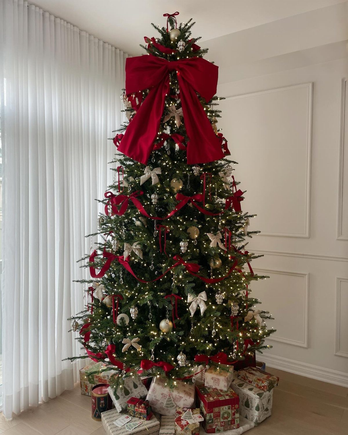 All Red Christmas Tree Decorations: 7 Ideas for Monochrome Style 5 A decorated Christmas tree with warm lights, gold ornaments, and red ribbon garlands draped around it.