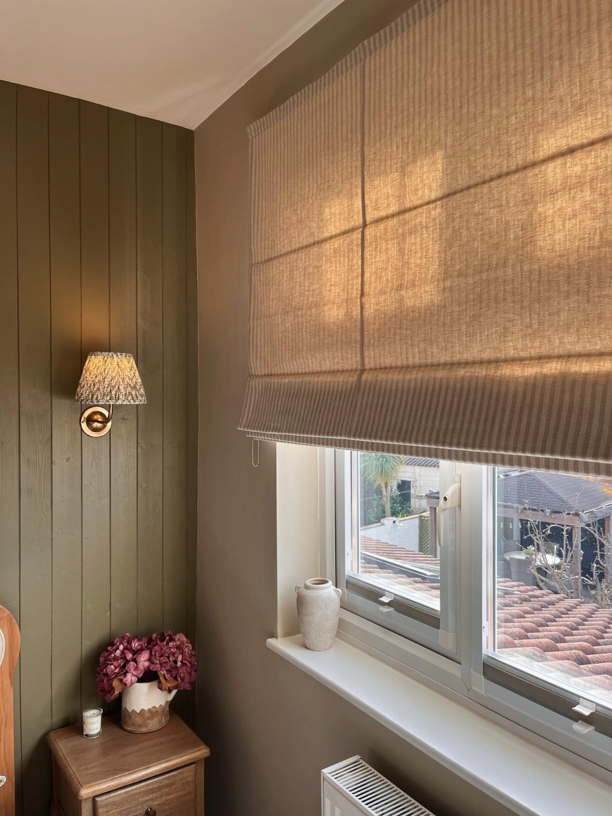 Beige fabric Roman shade covering a window with sunlight filtering through the textured material.