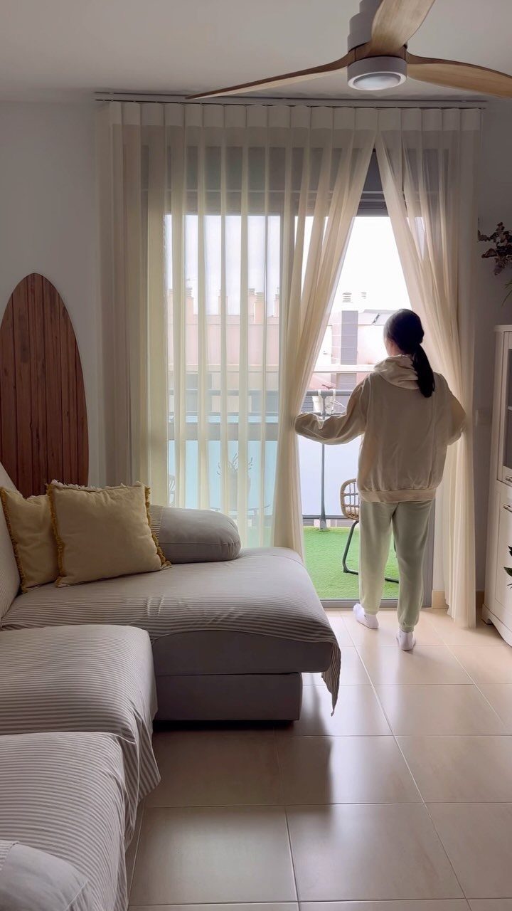 A person pulling back sheer vertical shades at a large glass door in a living room.