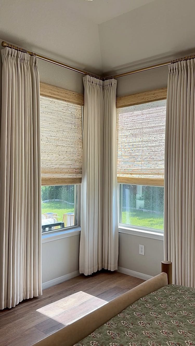 Woven bamboo shades paired with long white curtains hanging in a bright corner room.
