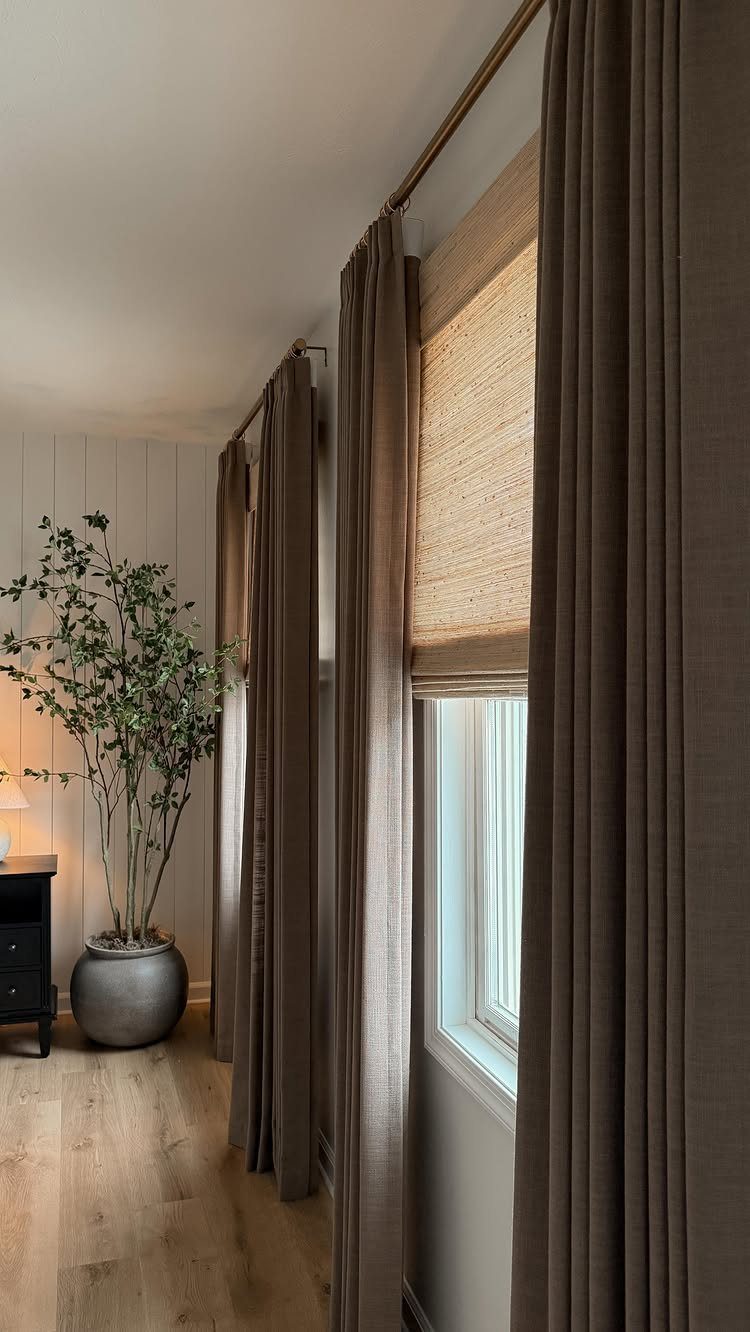 Brown curtains and tan bamboo shades hanging over windows in a bright room.