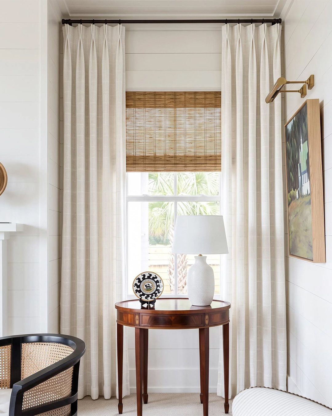 Woven bamboo shade framed by long cream linen curtains in a bright room.