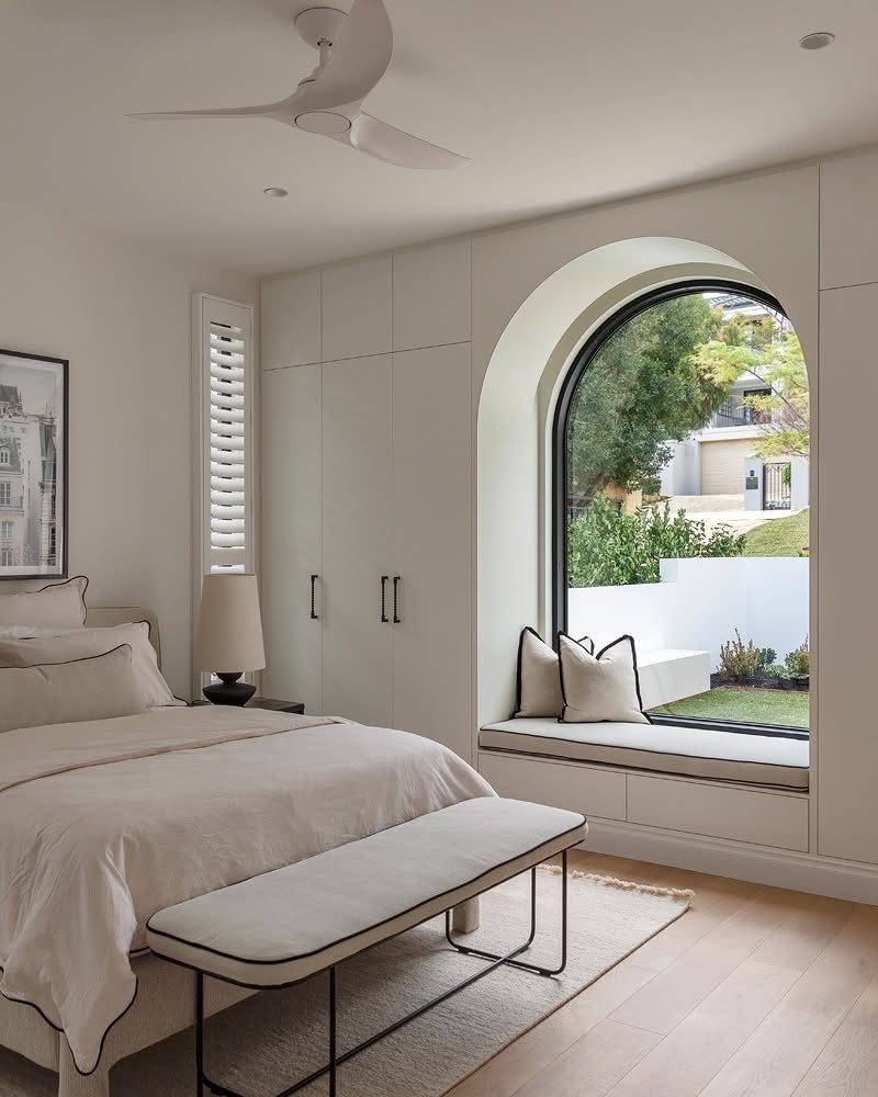 10 Bedroom Window Decor Ideas for Every Wall Height 2 An arched window with a black frame and a built-in window seat in a bright bedroom.