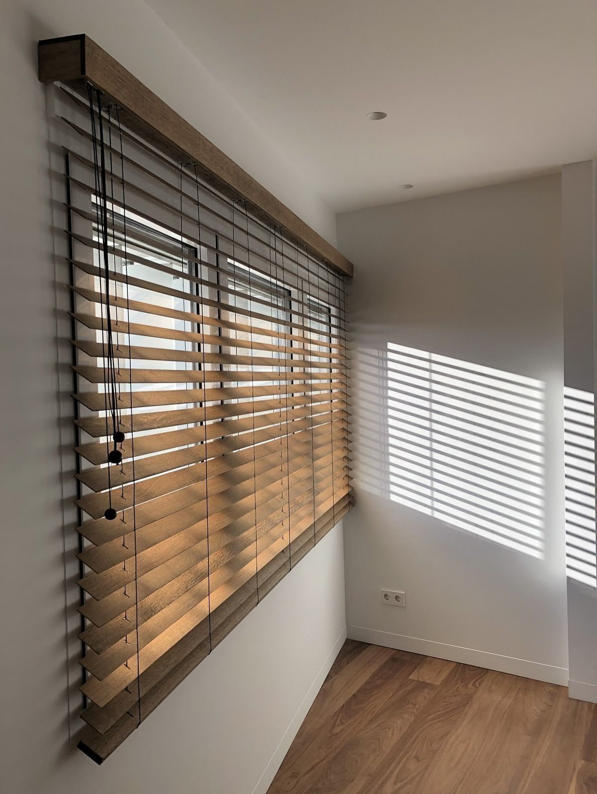 10 Bedroom Window Decor Ideas for Every Wall Height 8 Wooden horizontal blinds covering a large window in a bright, minimalist room with white walls.
