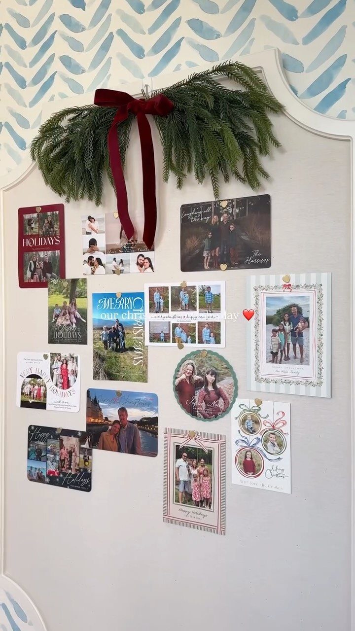 25 Christmas Decor Apartment Ideas That Maximize Space 13 Christmas cards pinned to a wall decorated with a green garland and a red velvet bow.
