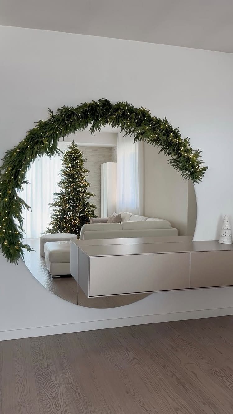 25 Christmas Decor Apartment Ideas That Maximize Space 22 A circular mirror decorated with a lighted green garland reflecting a Christmas tree and sofa.