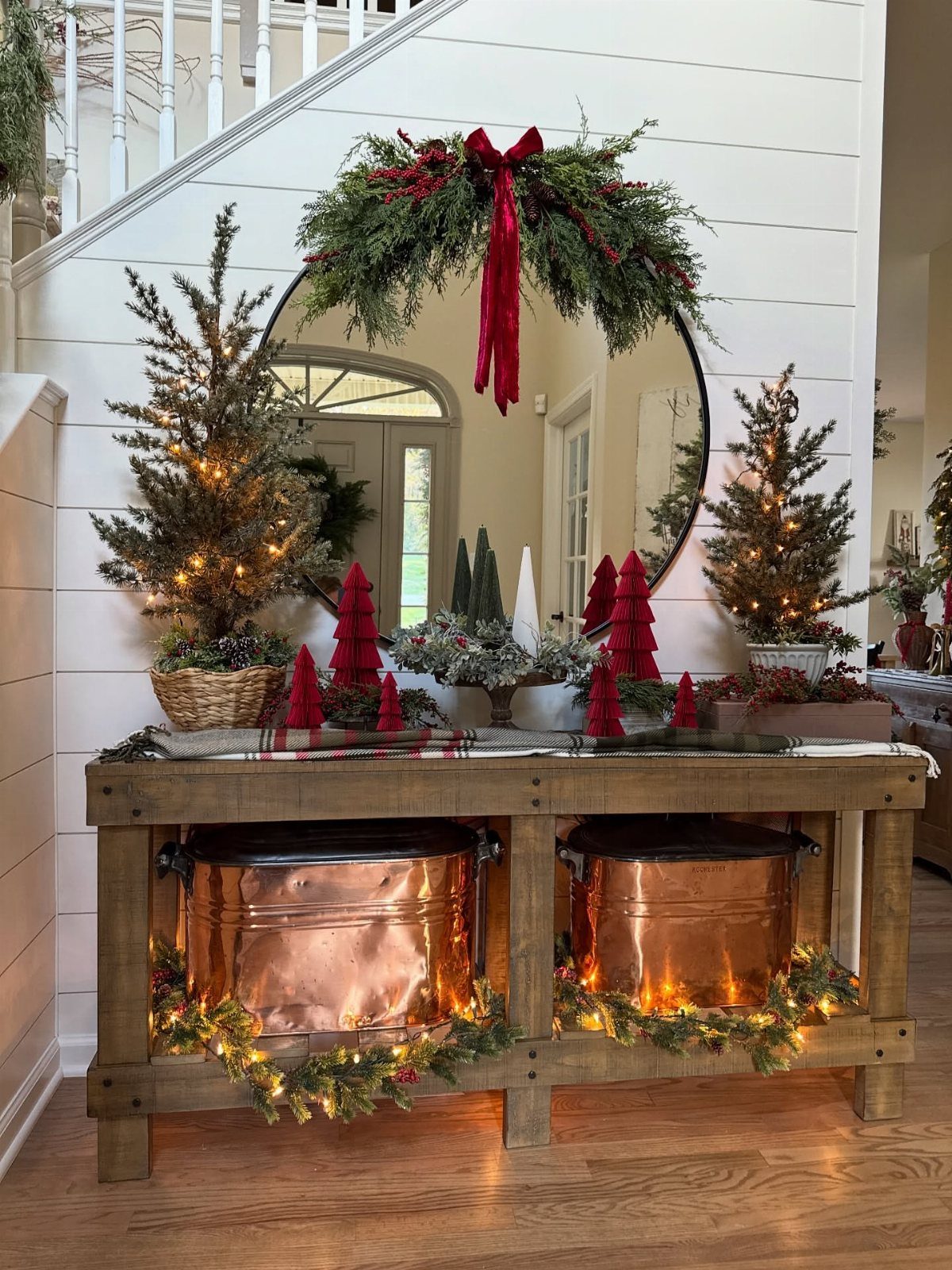 25 Christmas Decor Apartment Ideas That Maximize Space 15 A wooden console table decorated with small Christmas trees, greenery, and copper pots against a white wall.
