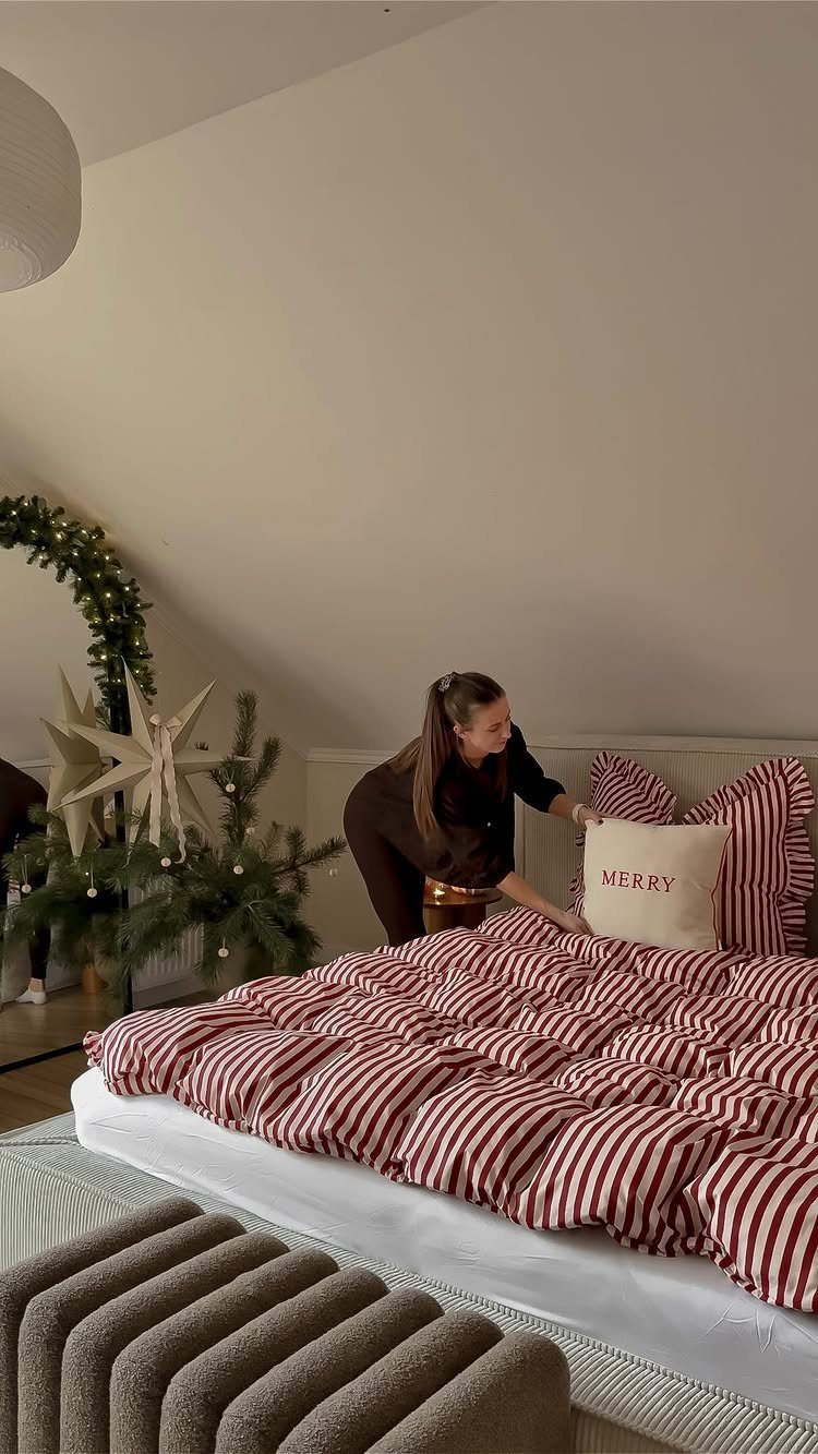 25 Christmas Decor Apartment Ideas That Maximize Space 2 A woman placing a white Merry Christmas pillow onto a red and white striped bed.