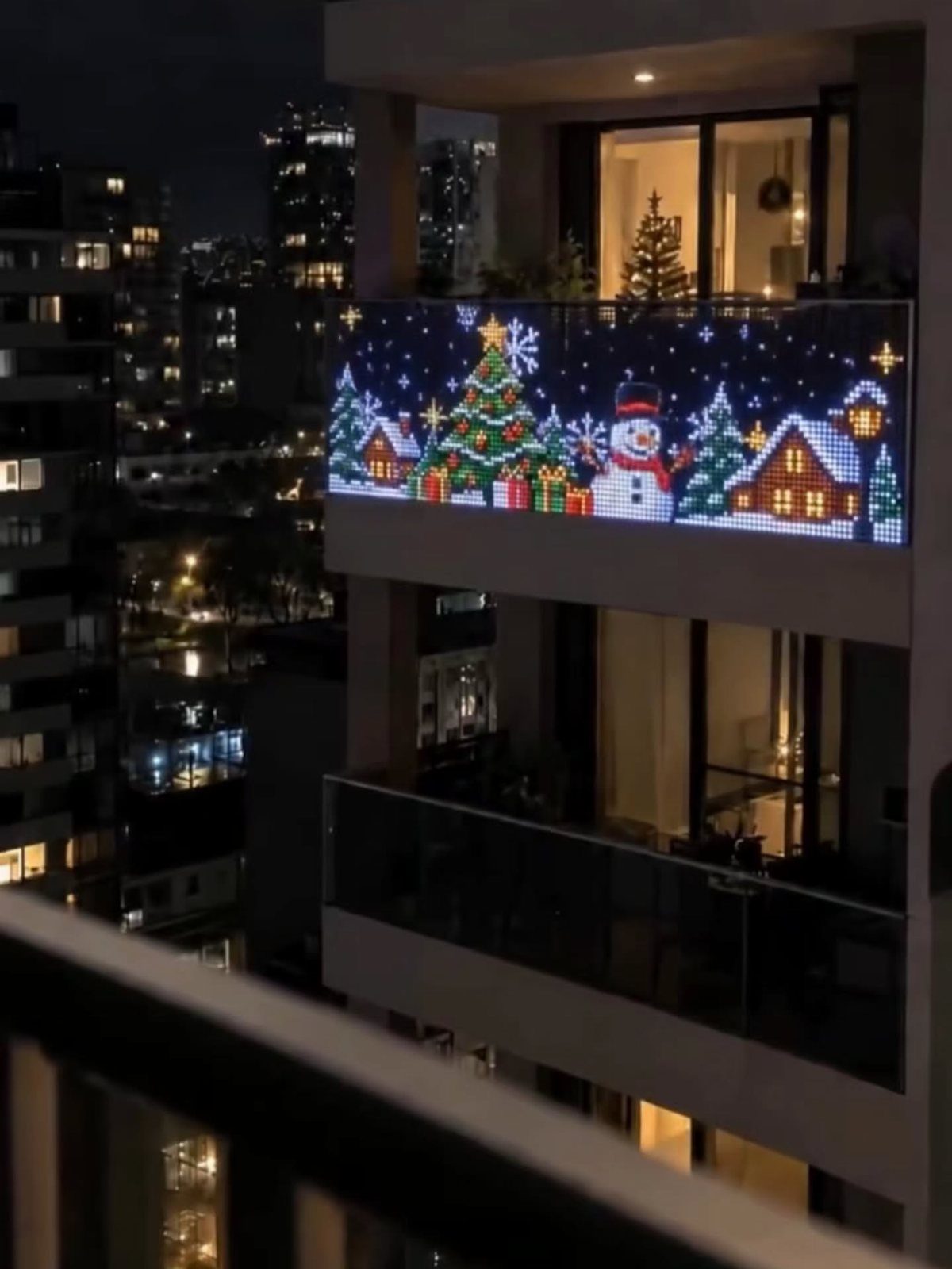 25 Christmas Decor Apartment Ideas That Maximize Space 25 An illuminated Christmas scene panel decorating an apartment balcony overlooking a city at night.