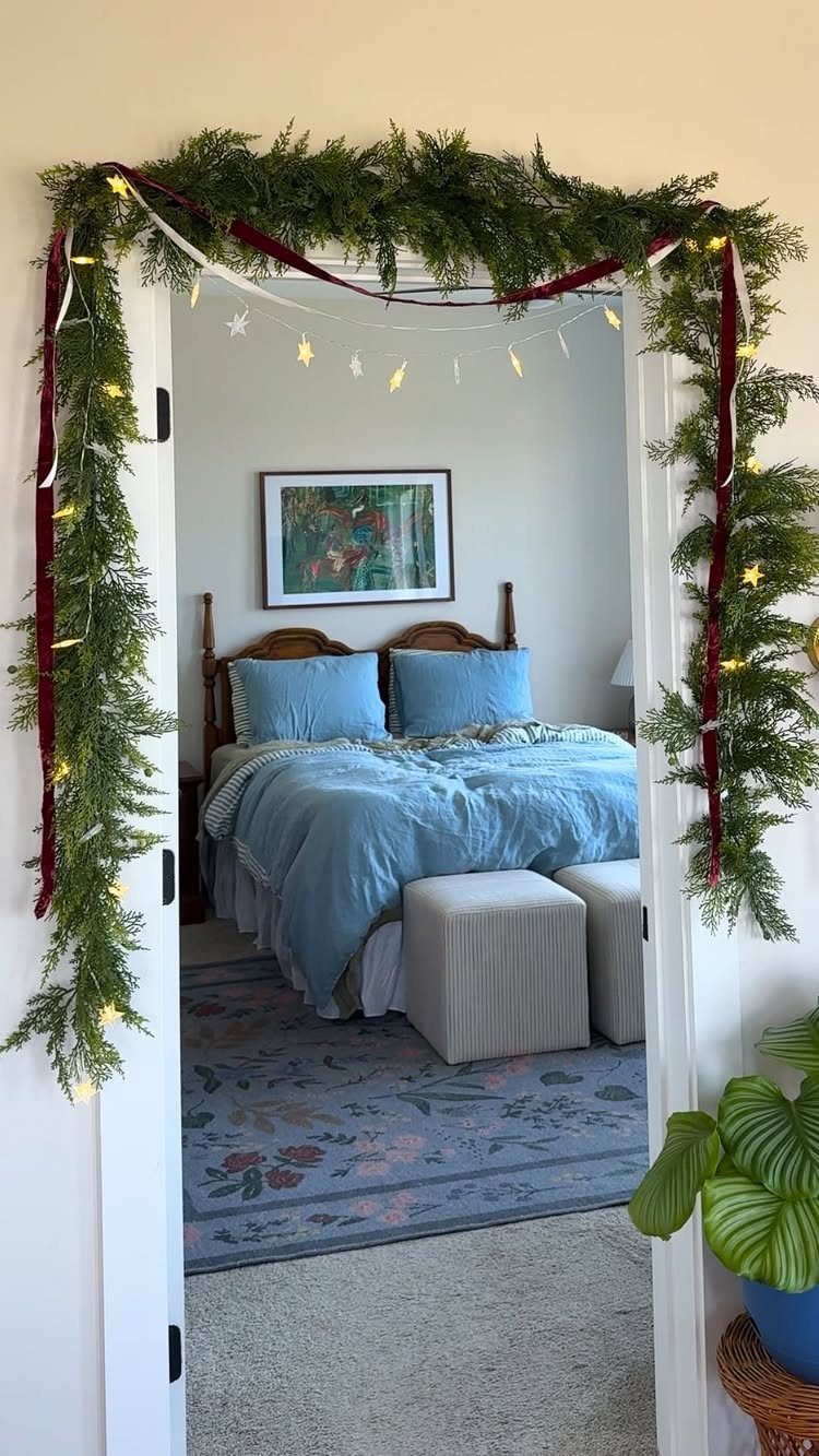 25 Christmas Decor Apartment Ideas That Maximize Space 12 Green evergreen garland with red ribbon and lights draped over a white doorway leading to a bedroom.