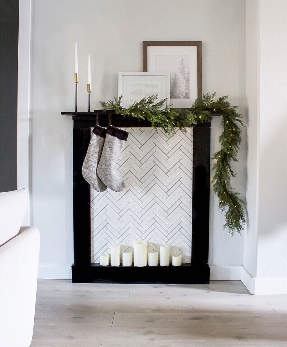 25 Christmas Decor Apartment Ideas That Maximize Space 6 A black decorative mantelpiece adorned with greenery, stockings, and white pillar candles against a light wall.