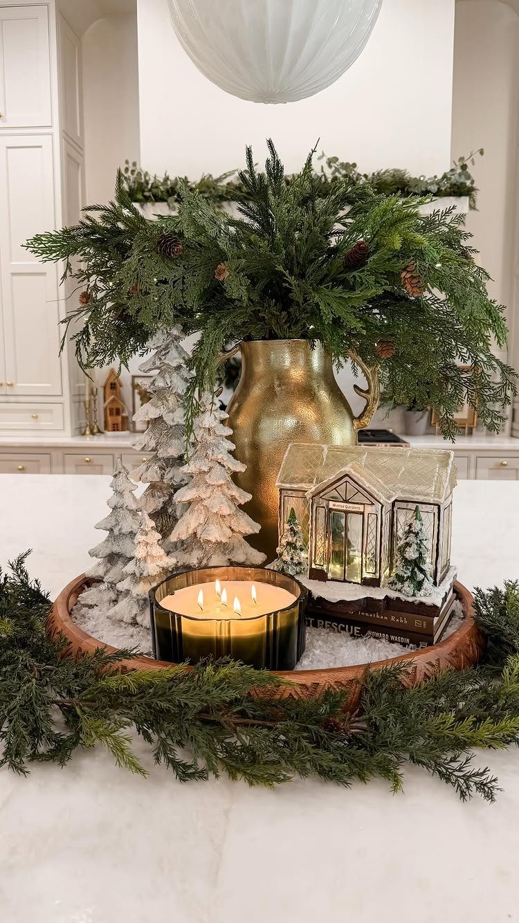 25 Christmas Decor Apartment Ideas That Maximize Space 24 Festive Christmas centerpiece with evergreen branches, gold pitcher, miniature houses, and a glowing candle on marble.