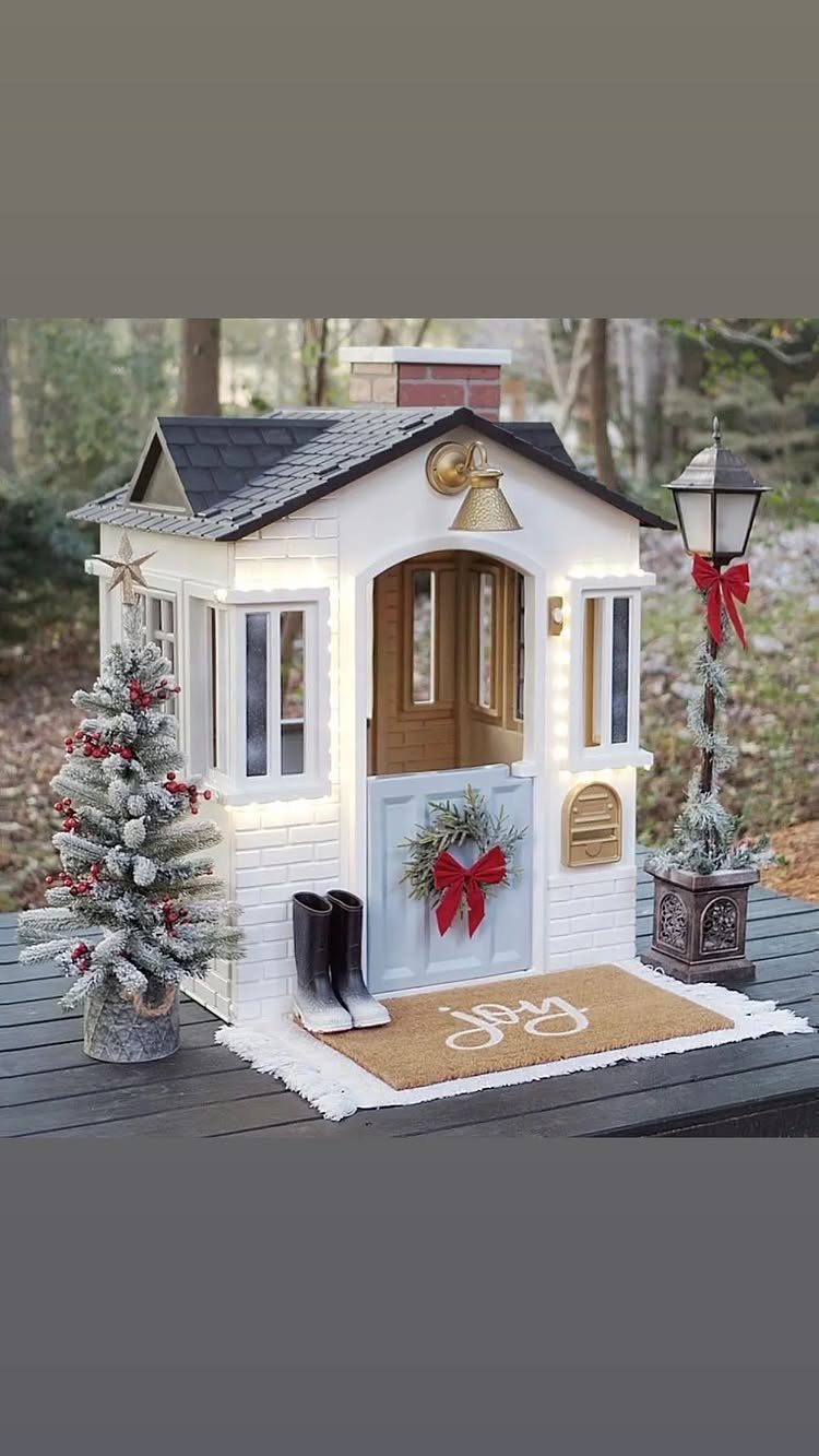 21 Christmas Decor Inspiration Ideas for Your Whole Home 2026 6 A white miniature playhouse decorated with a small Christmas tree, a wreath, and a joy doormat.
