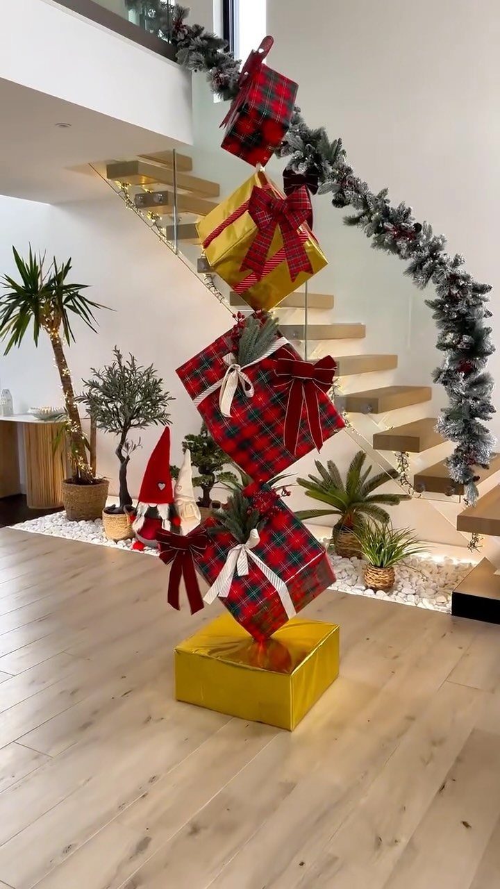 21 Christmas Decor Inspiration Ideas for Your Whole Home 2026 9 Large oversized gift boxes stacked vertically near a staircase decorated with evergreen garland.