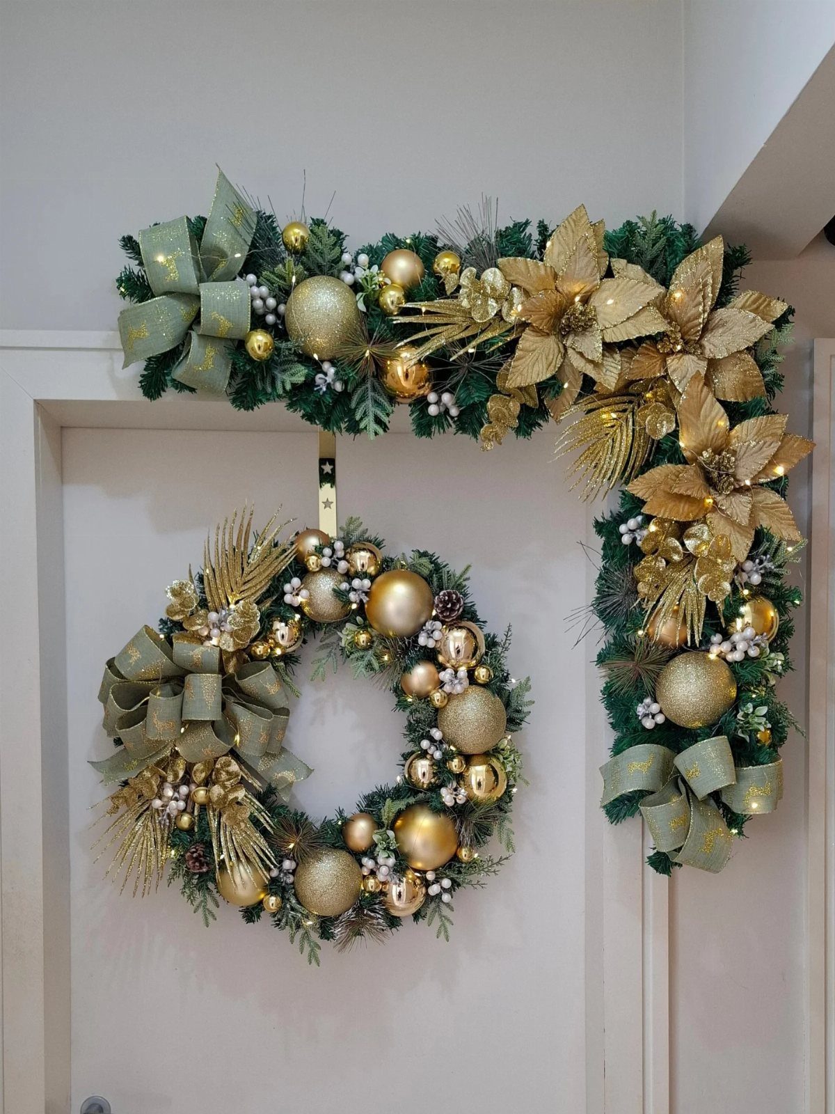 21 Christmas Decor Inspiration Ideas for Your Whole Home 2026 18 Gold and green holiday wreath and garland with ornaments and bows hanging on a white door.