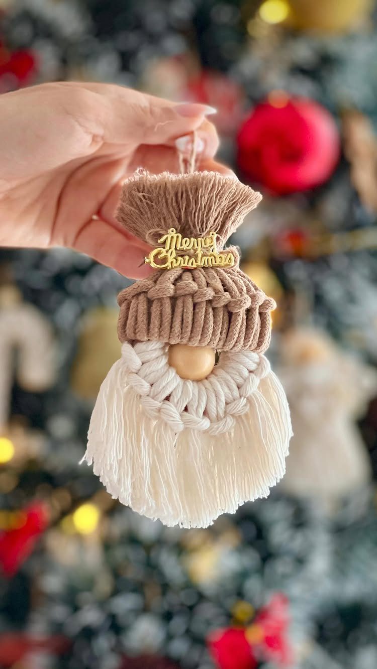 21 Christmas Decor Inspiration Ideas for Your Whole Home 2026 4 A hand holding a handmade macrame gnome ornament with a wooden Merry Christmas sign.