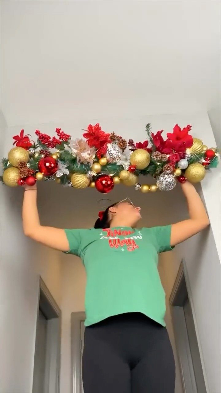 21 Christmas Decor Inspiration Ideas for Your Whole Home 2026 5 A person holding a festive garland of red and gold ornaments and poinsettias above their head.