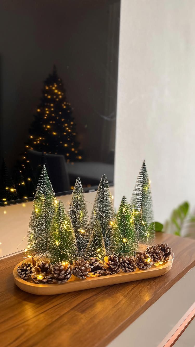 21 Christmas Decor Inspiration Ideas for Your Whole Home 2026 19 Small frosted pine trees with twinkling lights and pinecones on a wooden tray.