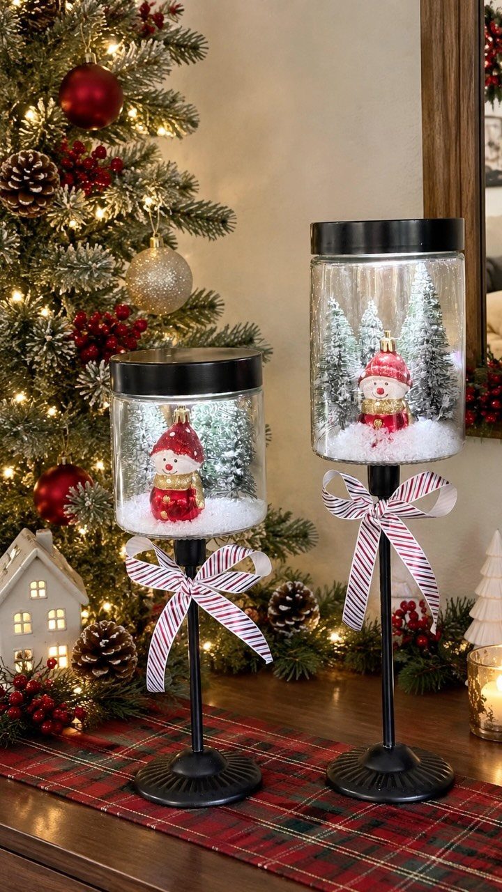 11 Christmas Home Decorating Ideas for 2026: Garlands to Lanterns 3 Two glass jars filled with snow, miniature trees, and Santa figurines on black stands.