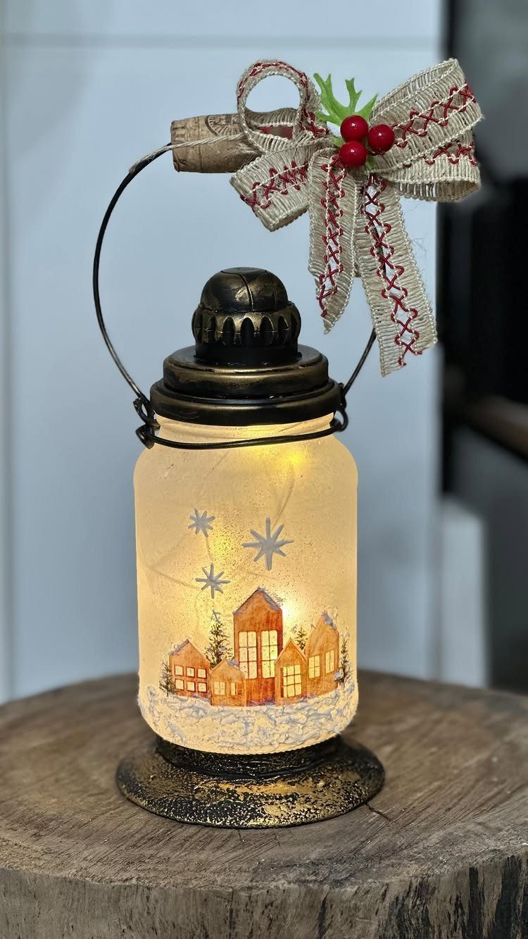 11 Christmas Home Decorating Ideas for 2026: Garlands to Lanterns 10 A glowing glass lantern jar decorated with a winter village scene and a burlap bow.