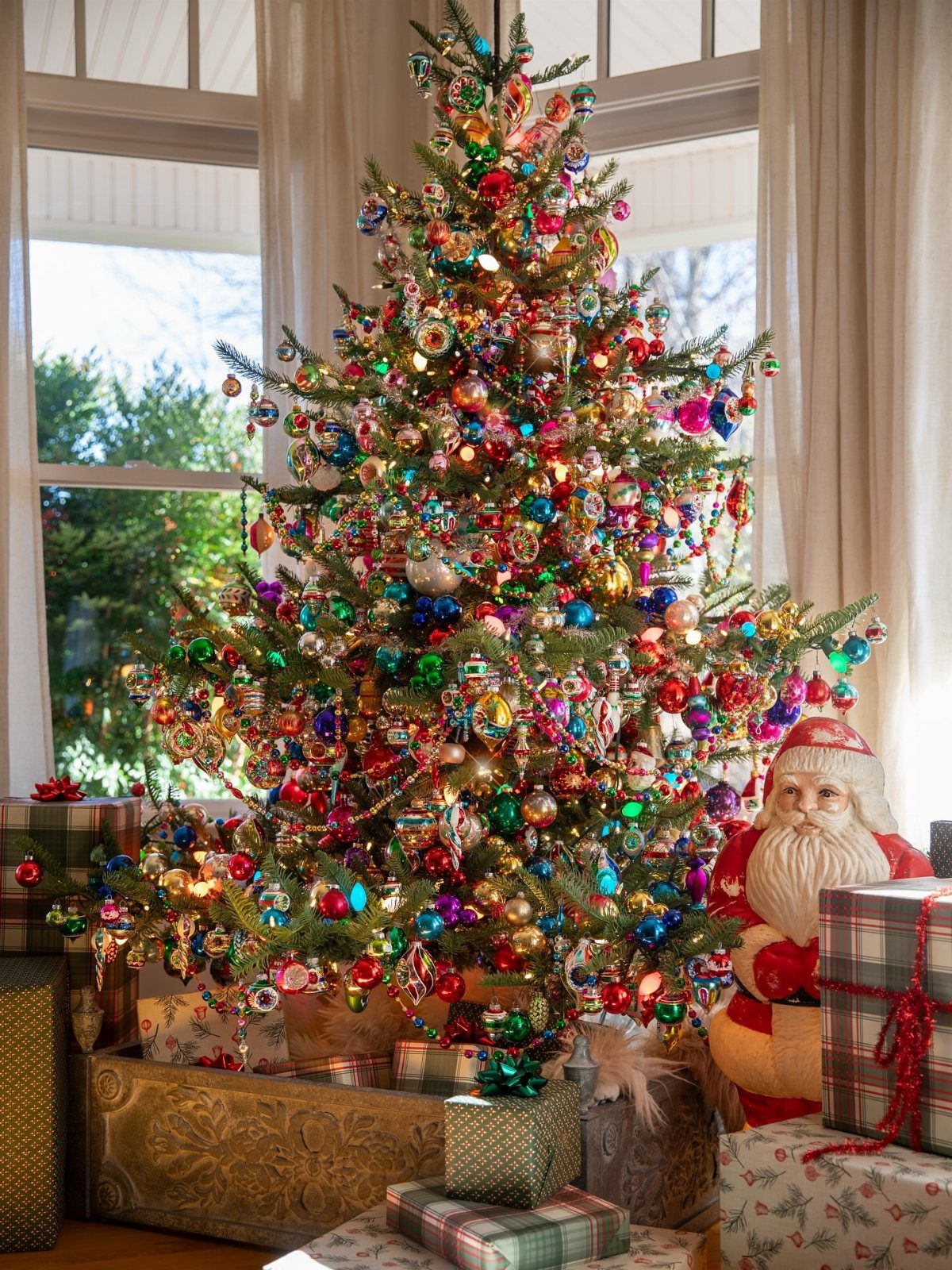 11 Christmas Home Decorating Ideas for 2026: Garlands to Lanterns 2 A decorated Christmas tree with colorful ornaments and lights surrounded by wrapped gifts.