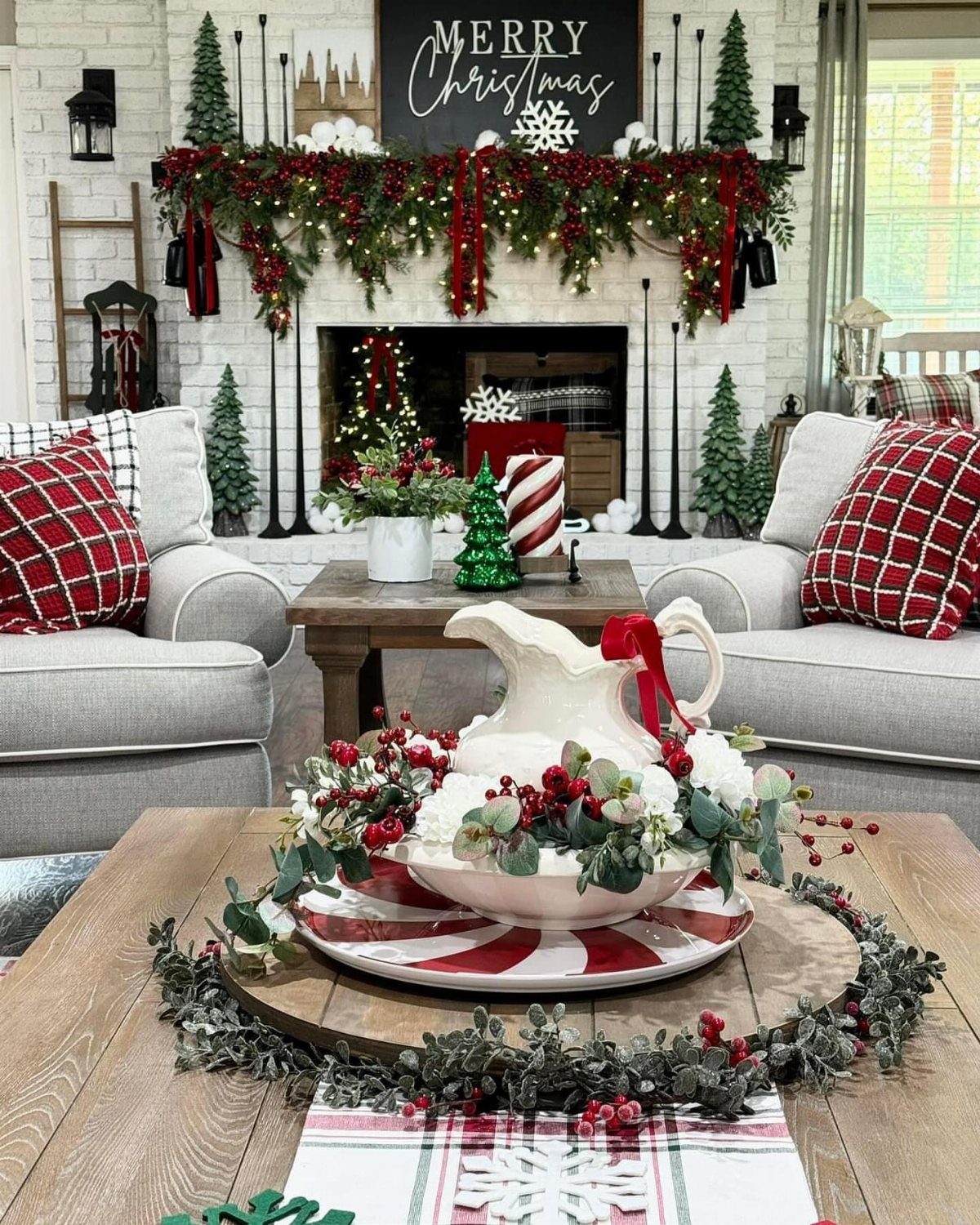A decorated Christmas mantel with green garland, red berries, and a Merry Christmas sign above a fireplace.