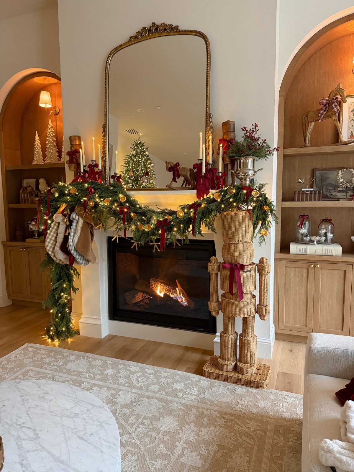 A decorated white fireplace mantel with green garland, lights, and a large gold mirror above it.