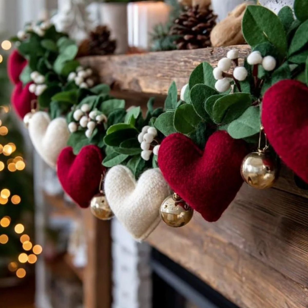 Greenery garland with red and white felt hearts and gold ornaments on a wooden mantel.