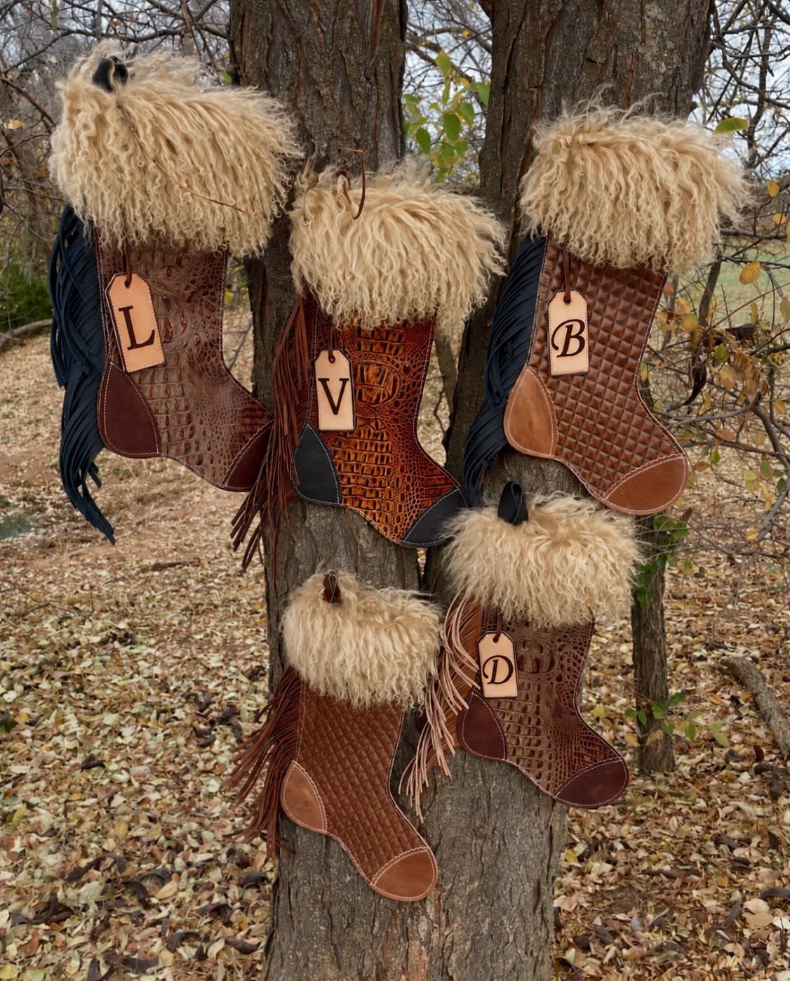 20 Christmas Rustic Decor Ideas for a Warm Holiday Home 16 Five leather cowboy boot stockings with fur trim hanging from a tree trunk outdoors.