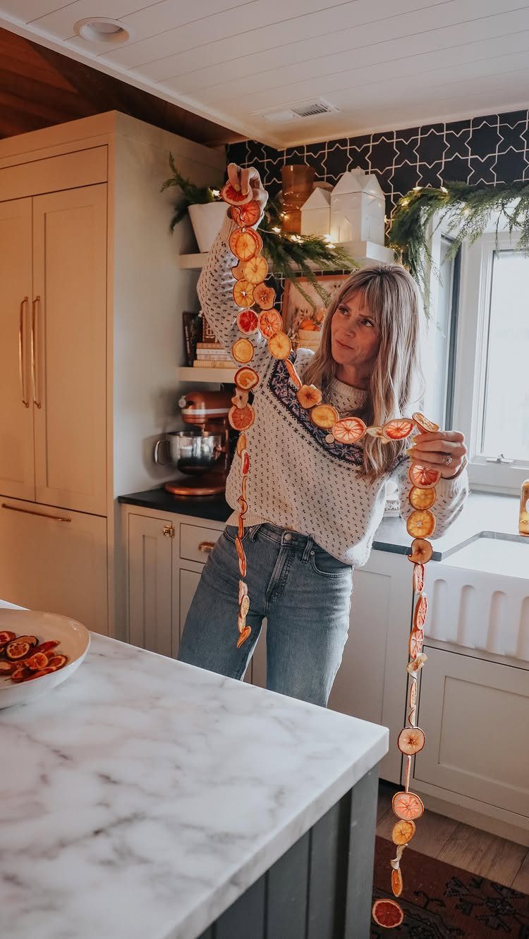 20 Christmas Rustic Decor Ideas for a Warm Holiday Home 19 A woman holding a long garland made of dried orange slices in a kitchen.