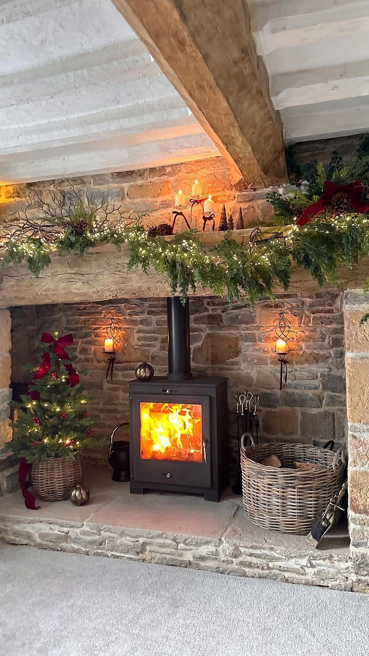 20 Christmas Rustic Decor Ideas for a Warm Holiday Home 17 Stone fireplace with a wood-burning stove, decorated with evergreen garland and fairy lights.