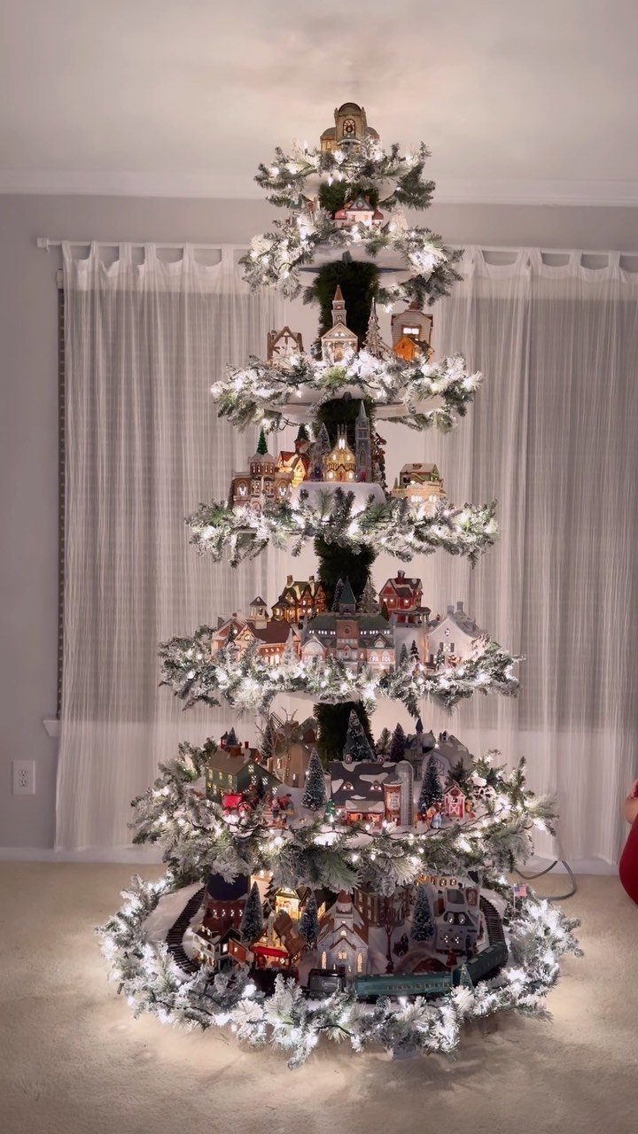 19 Christmas Village Ideas for Displaying a Miniature Scene 13 A Christmas tree featuring multiple tiers of miniature village houses and snowy pine branches.