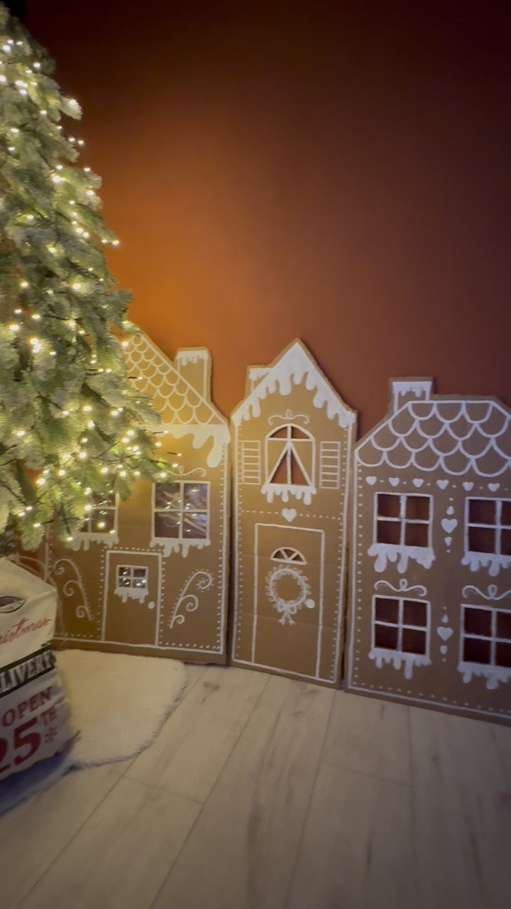 19 Christmas Village Ideas for Displaying a Miniature Scene 1 Cardboard cutout houses with white decorative patterns standing next to a glowing Christmas tree.