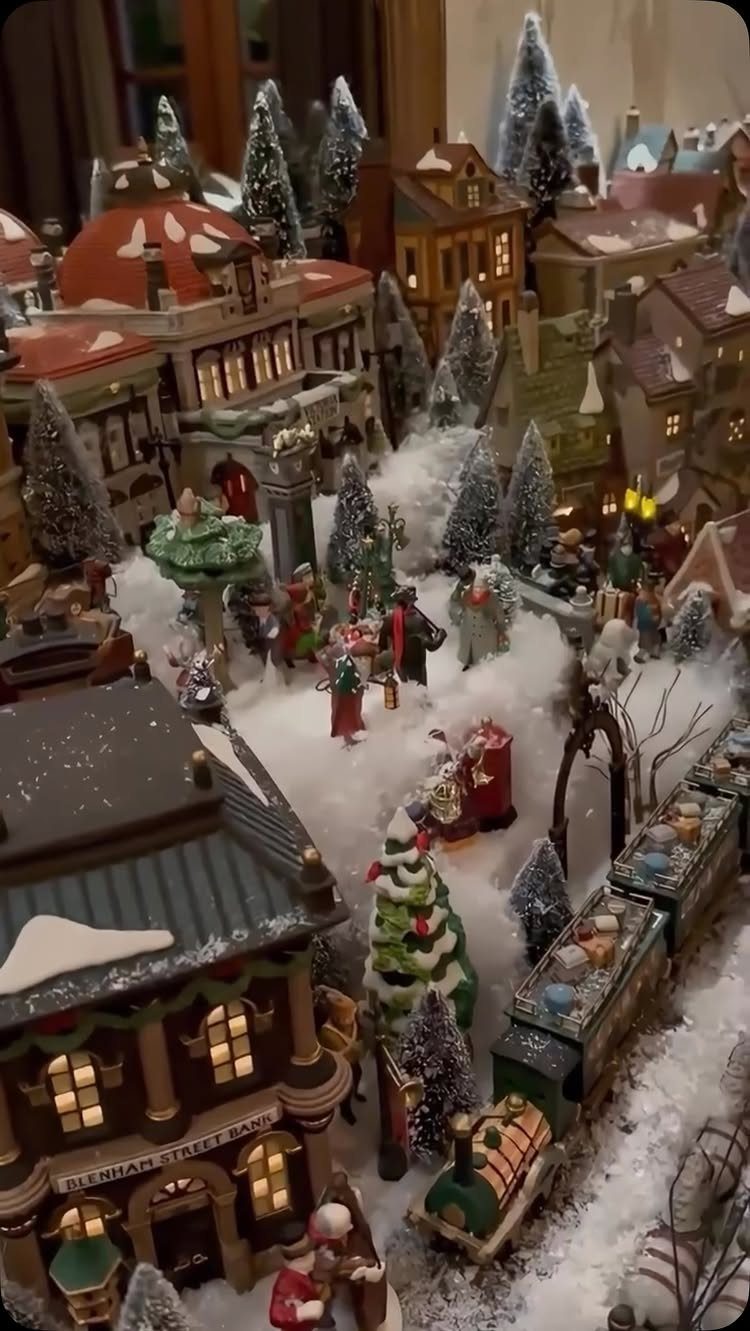 19 Christmas Village Ideas for Displaying a Miniature Scene 4 Miniature Christmas village houses and figurines arranged on white cotton batting snow.