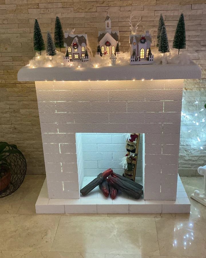 19 Christmas Village Ideas for Displaying a Miniature Scene 12 Miniature Christmas village houses and pine trees displayed on a white brick fireplace mantel.