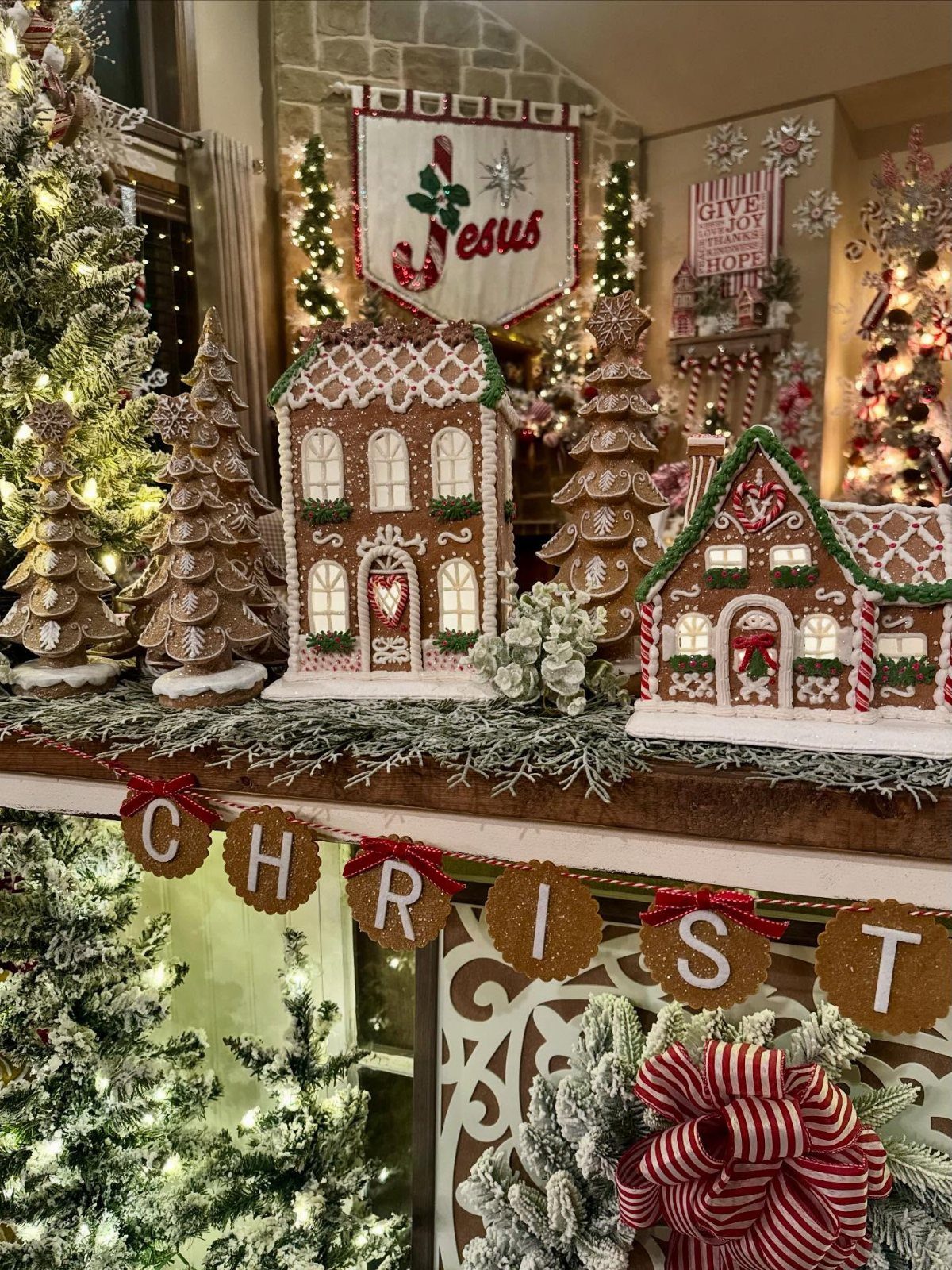 19 Christmas Village Ideas for Displaying a Miniature Scene 3 Decorated gingerbread houses and miniature trees arranged on a festive mantelpiece with greenery.