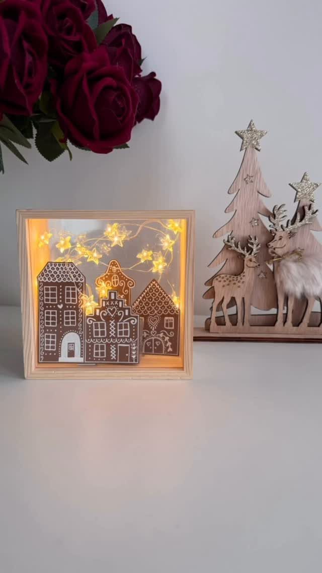 19 Christmas Village Ideas for Displaying a Miniature Scene 18 Miniature illuminated gingerbread houses inside a wooden shadow box next to wooden reindeer decorations.