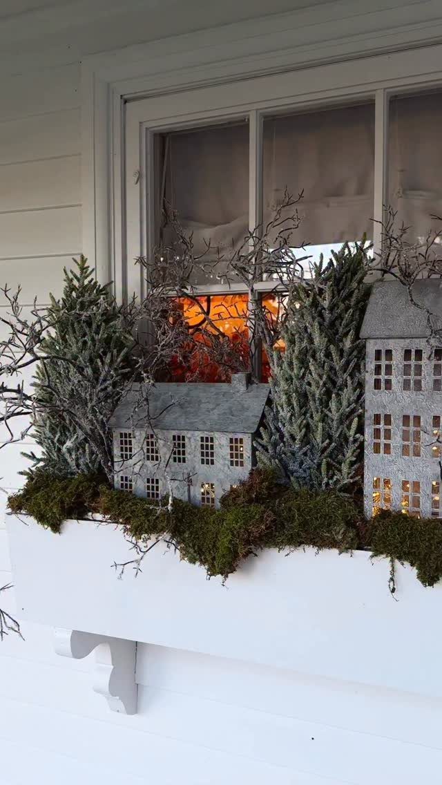 19 Christmas Village Ideas for Displaying a Miniature Scene 15 Miniature lit ceramic houses and evergreen trees arranged in a white window box with moss.