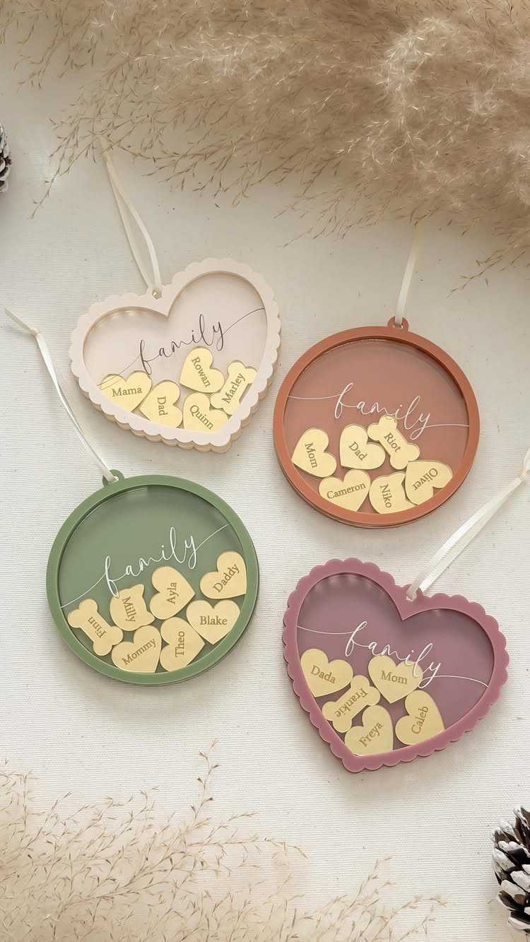 Four pastel-colored shaped ornaments containing small gold heart tags with names inside clear frames.