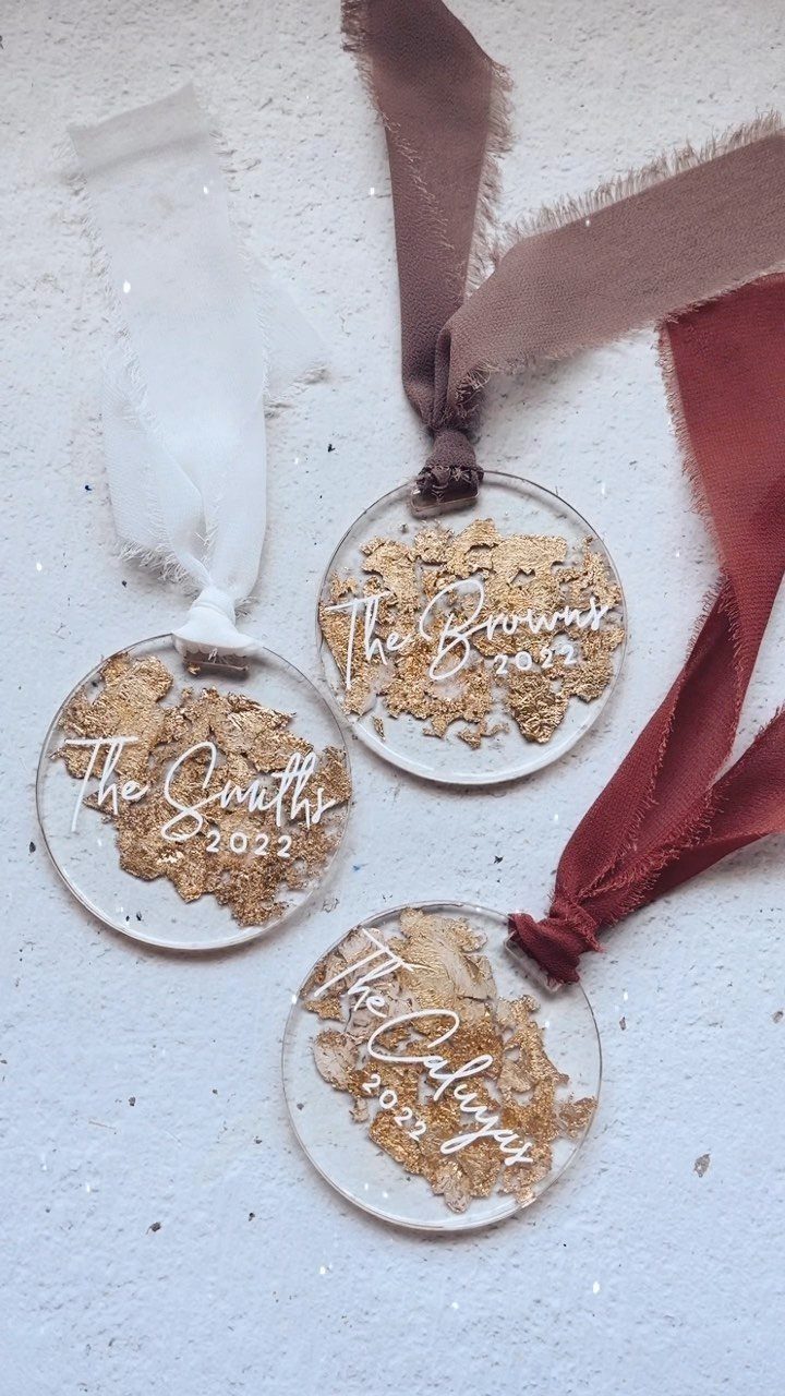 Three clear acrylic ornaments with gold flakes and white cursive lettering on a white background.
