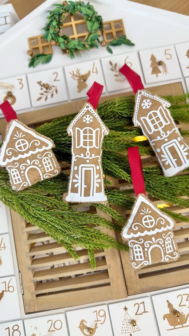 Gingerbread house shaped felt ornaments with white stitching resting on green evergreen branches.