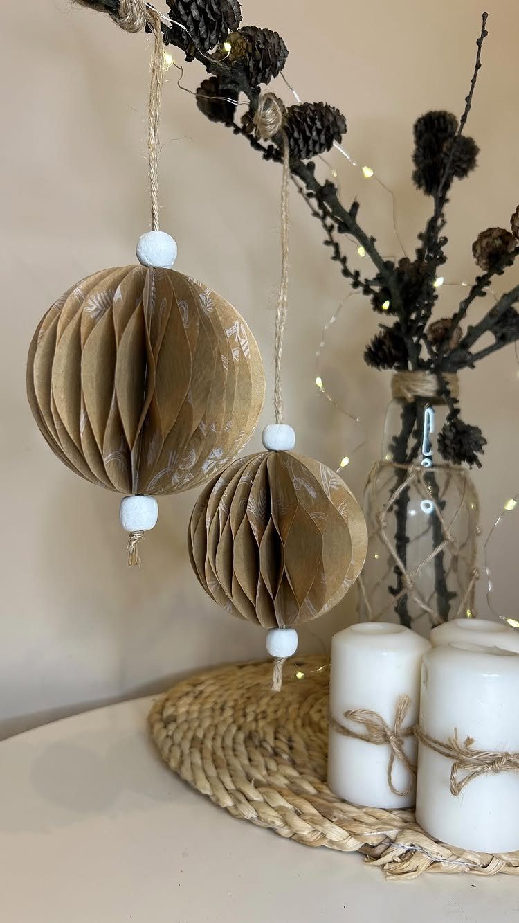 Two brown honeycomb paper ornaments hanging from a branch near white candles.