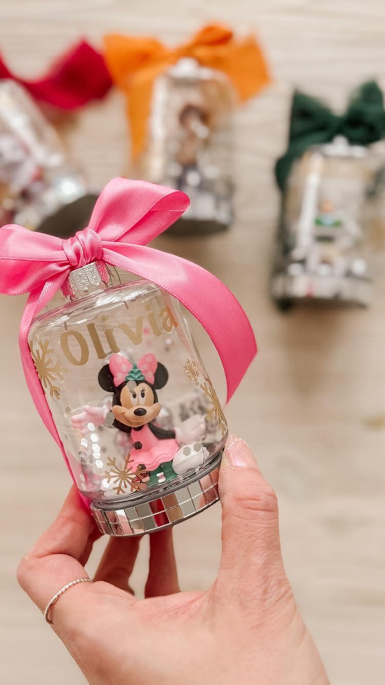 A hand holding a clear bell-shaped ornament with Minnie Mouse and a pink bow.
