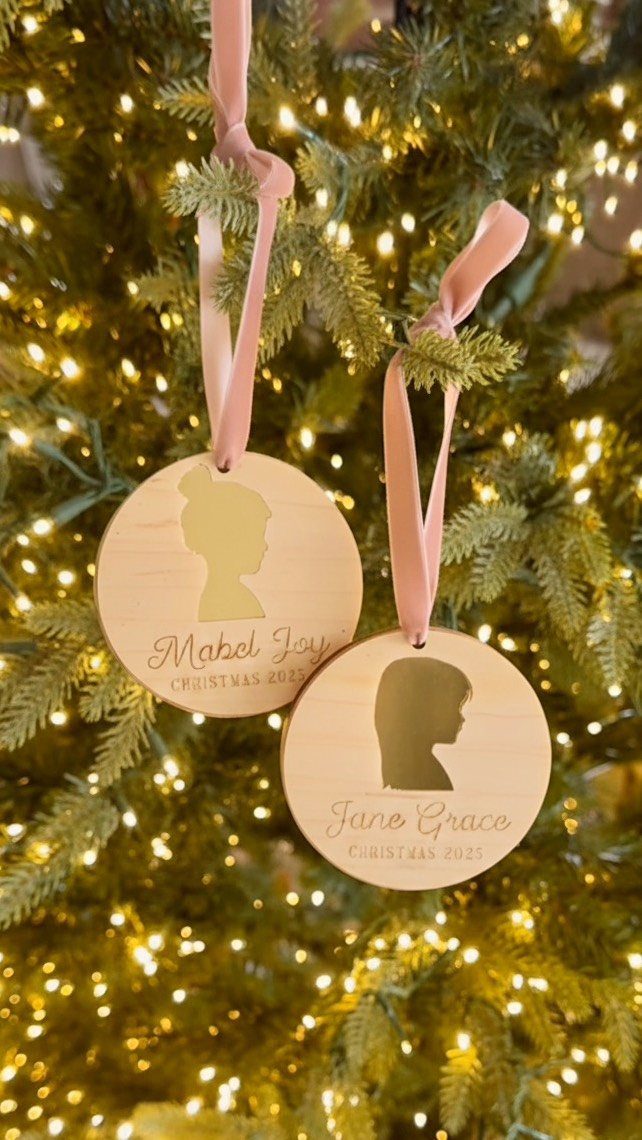 Two personalized wooden ornaments with child silhouettes hanging on a glowing Christmas tree.