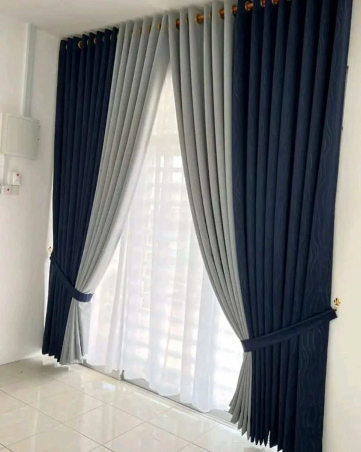 Navy blue and grey curtains hanging over a window with white sheer fabric underneath.