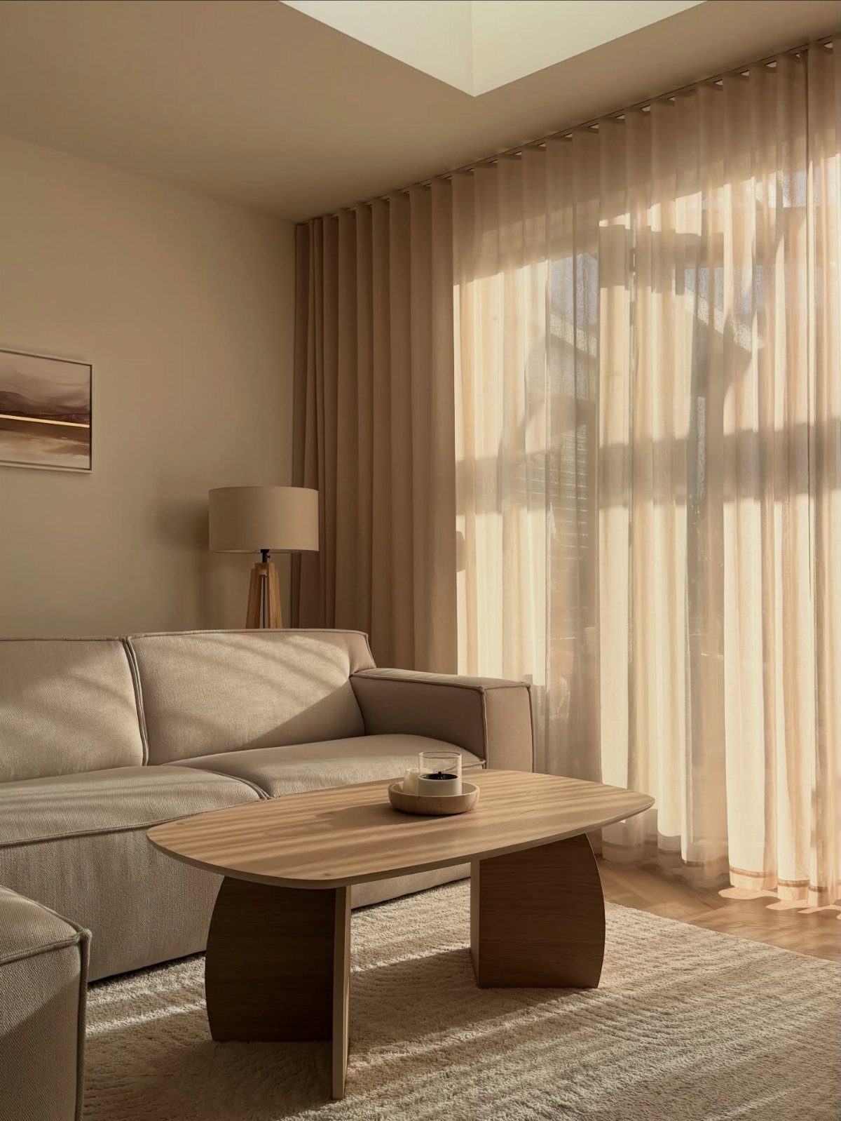 Sheer beige curtains hanging in a sunlit modern living room with a neutral sofa.