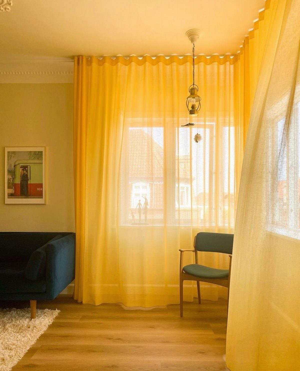 Sheer yellow curtains hanging over a large window in a bright living room.